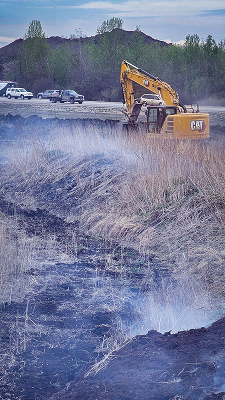 Hi-Tower excavator working through smoke to contain the Poundmaker peat fire near Anthony Henday Drive in west Edmonton, May 2025.